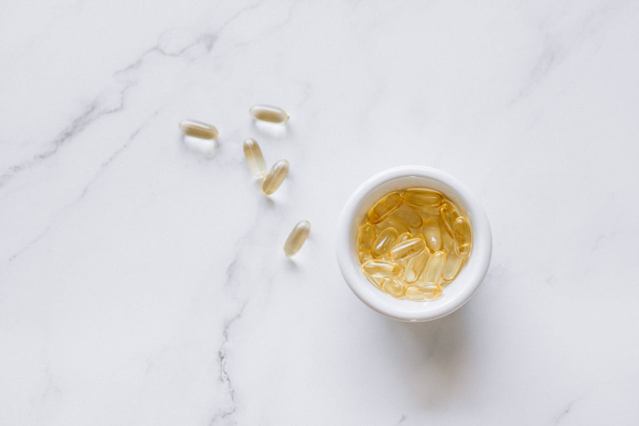 Top view of scattered capsules and a bowl on a marble surface, minimalistic setup.